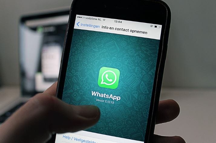 Como mandar mensagem automática no WhatsApp: imagem de uma mão segurando o celular com a tela do WhatsApp aberta.