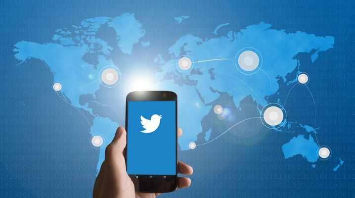 Twitter Trending Topics: imagem de uma mão segurando um celular com a logo do twitter na tela e a imagem de um mapa mundi no fundo em azul.