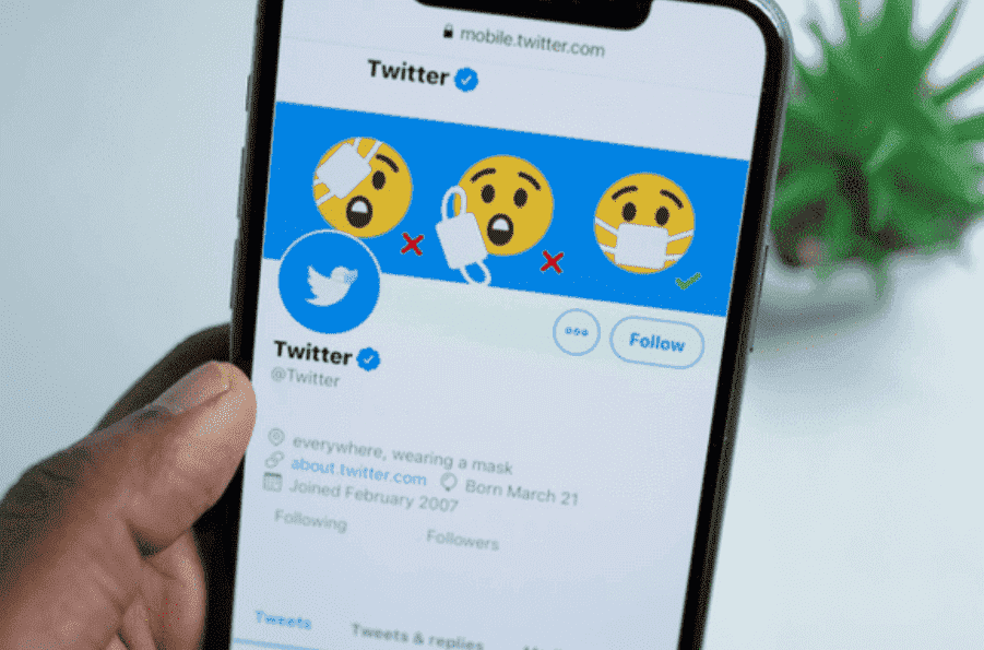 Capa para Twitter header: uma mão branca está segurando um celular ligado na página principal do Twitter, no qual podemos ver a foto da capa e do perfil.